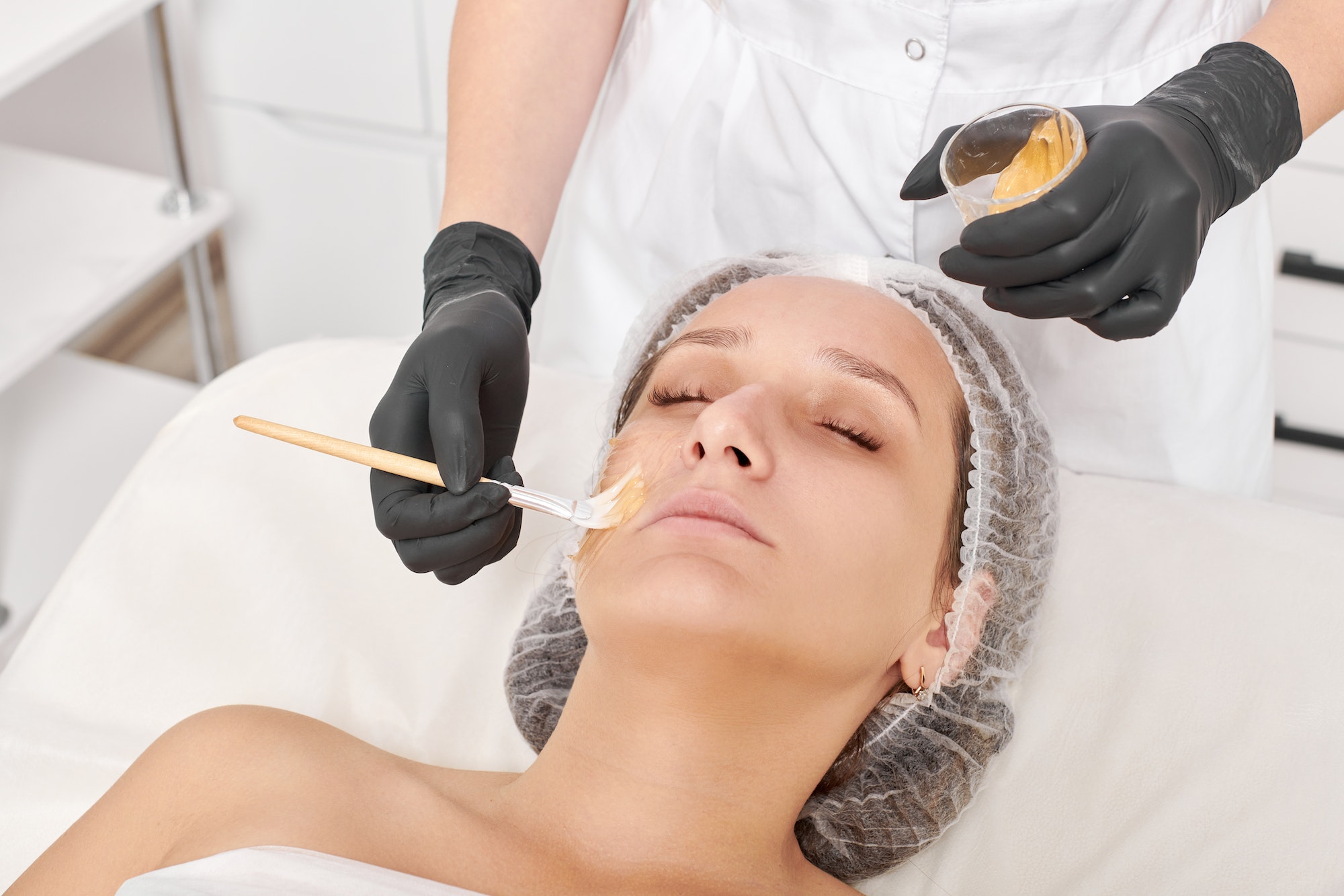 Cosmetologist applies honey mask on woman face for moisturize face skin in beauty spa salon